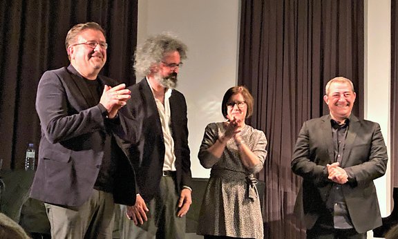 Vier Personen stehen auf der Bühne, drei davon applaudieren.