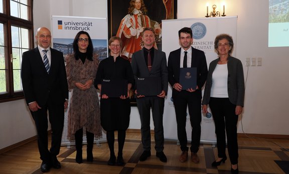 Sechs Personen stehen für ein Gruppenfoto nebeneinander, hinter ihnen sind Roll-ups mit den Logos der Universitäten.